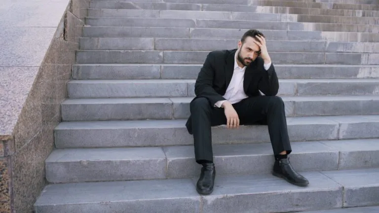 Man in suit sitting on outdoor stairs looking down.