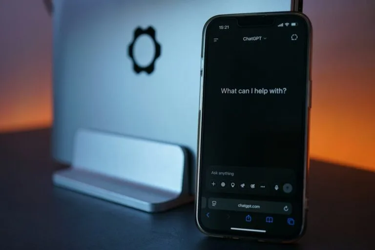 Phone displays chatgpt, next to laptop.