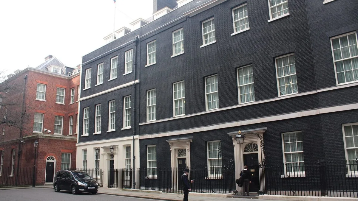 Budynek 10 Downing Street w Londynie, siedziba premiera Wielkiej Brytanii. Przed wejściem stoi mężczyzna, obok zaparkowany…
