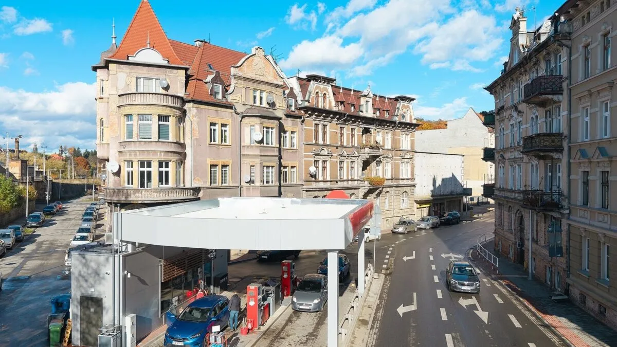 Stacja paliw Orlen w Kłodzku; samochody tankują przy dystrybutorach pod białym zadaszeniem, obok kamienic.