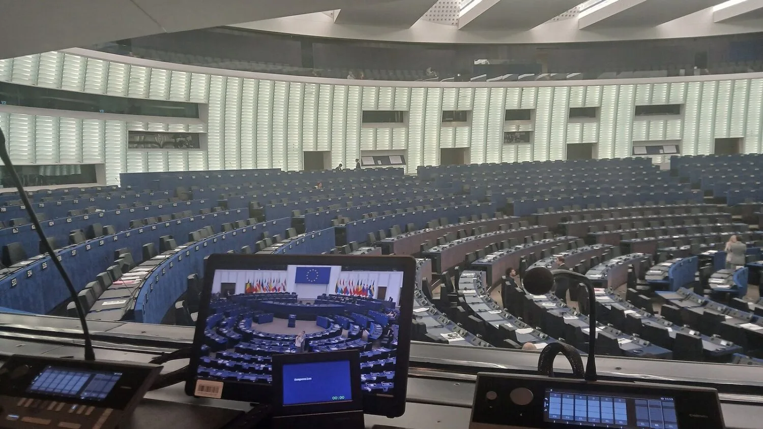 Sala plenarna Parlamentu Europejskiego w Strasburgu widziana z kabiny tłumaczy; na ekranie widać obrady, a wokół rzędy…