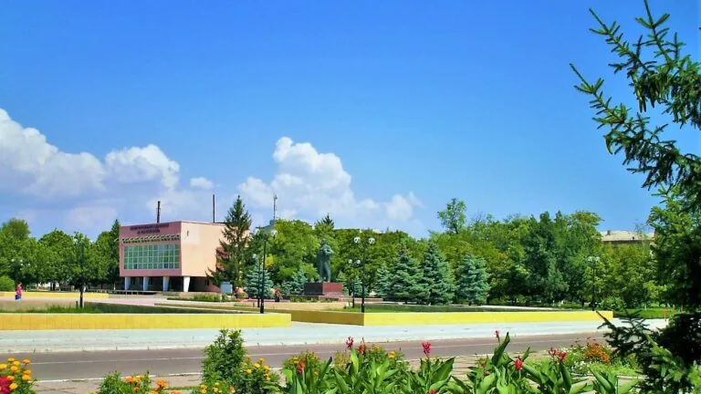 Centralny plac w Ołeszkach z pomnikiem, budynkiem i zielenią w letni, słoneczny dzień