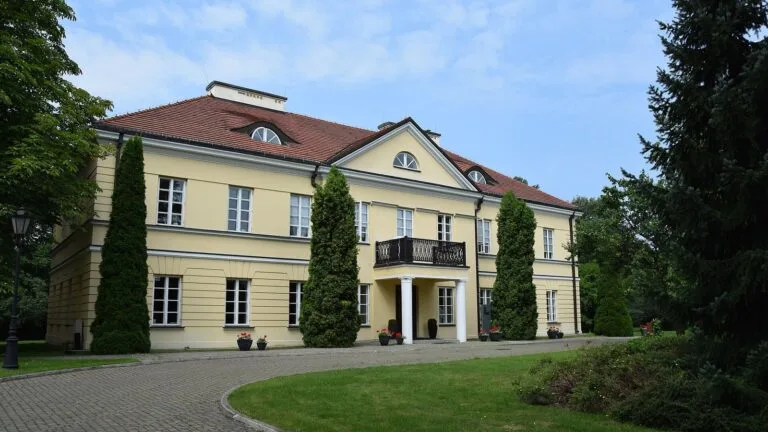 Żółty, klasycystyczny budynek z balkonem i podjazdem wśród drzew, siedziba Konfederacji Lewiatan w Warszawie.