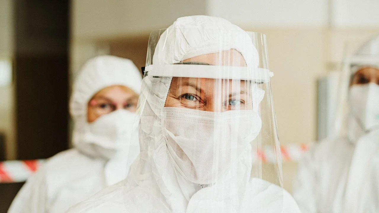 Osoba w białym kombinezonie ochronnym, masce i przyłbicy, ilustracja pracy personelu medycznego podczas epidemii.