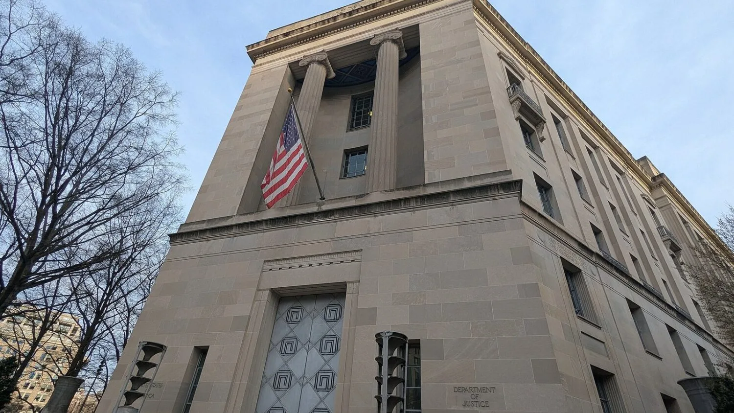 Gmach Departamentu Sprawiedliwości USA w Waszyngtonie z amerykańską flagą na fasadzie.