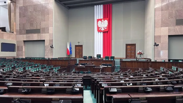 Sala posiedzeń Sejmu RP z pustymi ławami poselskimi i godłem Polski na ścianie