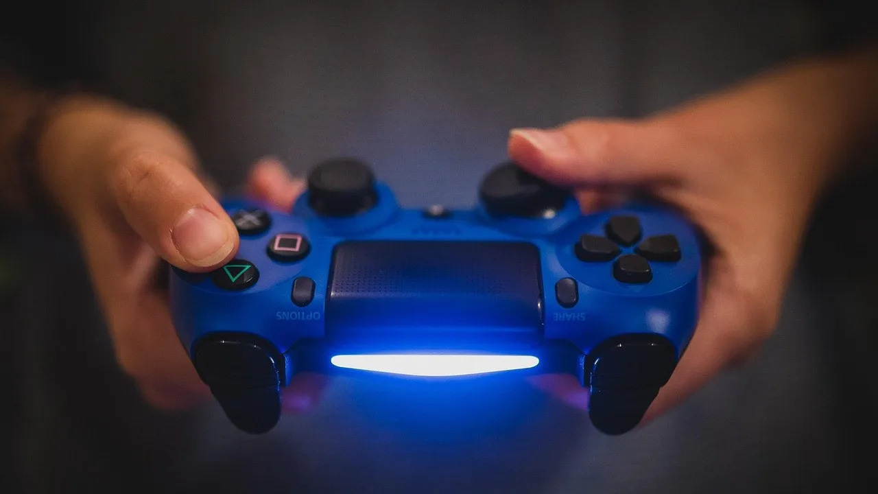 Dłonie trzymające niebieski pad do PlayStation z podświetloną diodą na ciemnym tle