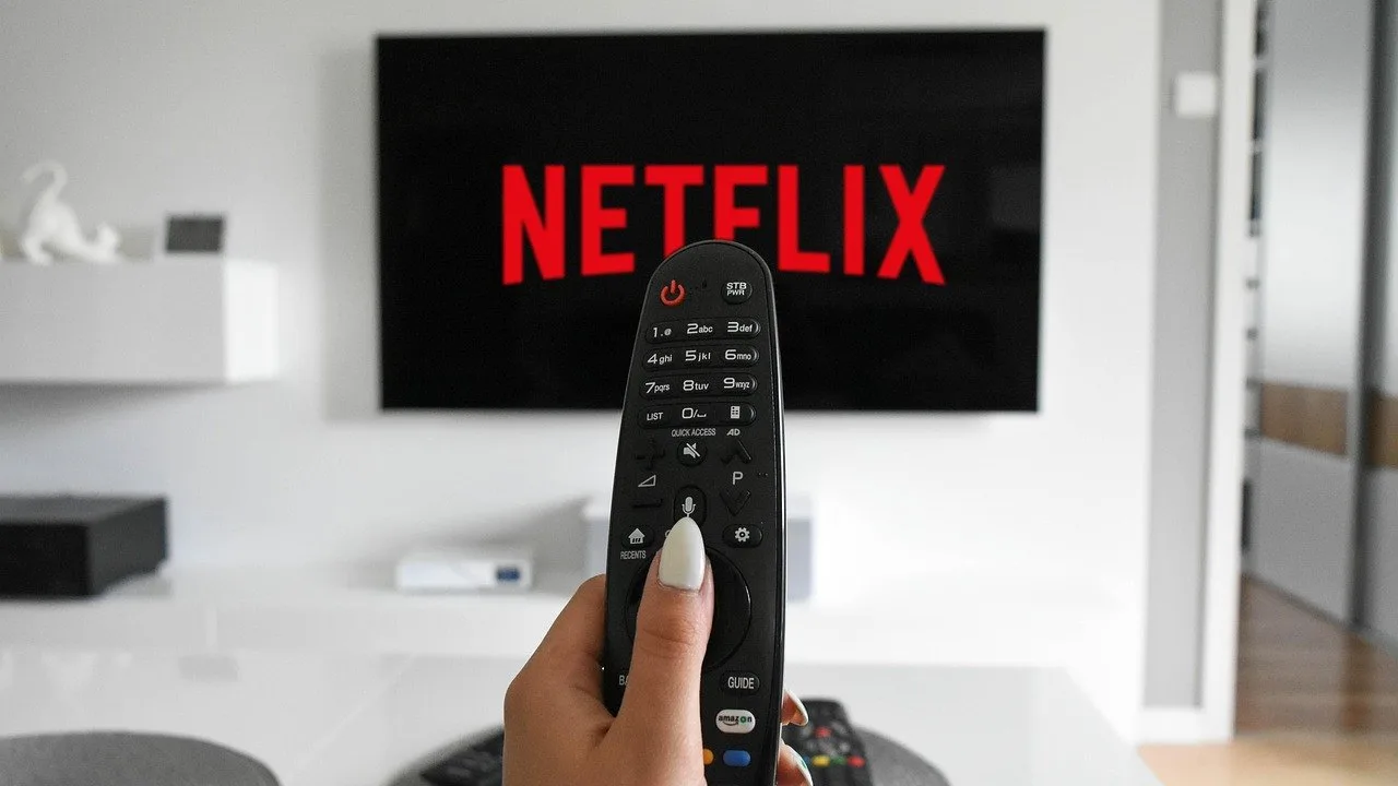 Osoba trzyma pilot przed telewizorem, na którym widać logo Netflixa.