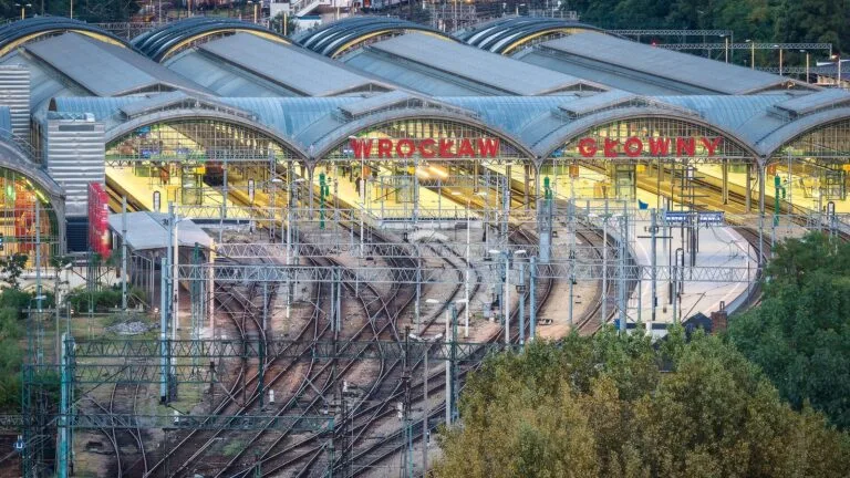 Widok z góry na perony i tory Dworca Głównego we Wrocławiu, z napisem „Wrocław Główny” na szklanych wiatach.